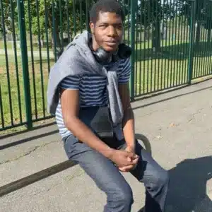 Un jeune déficient visuel est assis sur un banc dans une rue ensoleillée